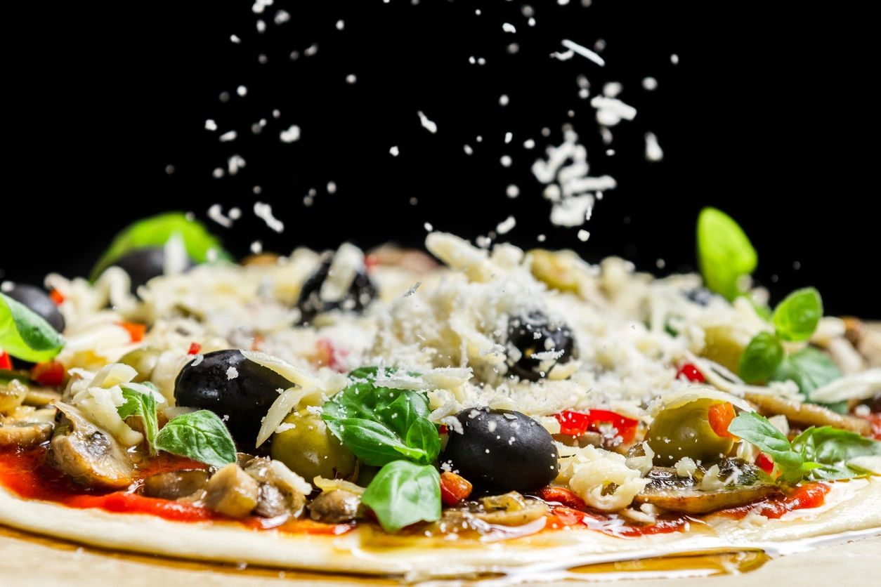 Falling cheese on a freshly prepared pizza with black olives